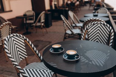 Arka plandaki masada iki güzel bardak cappuccino. Mükemmel kalp şeklinde latte sanatı. Kahve molası, kafede zaman geçirmek, rahatlamak ve sıcak içecek konseptinin tadını çıkarmak. Yan görünüm.