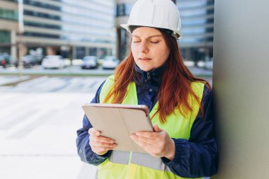 Beyaz kasklı ve güvenlik yeleği giyen genç mimar kadın dijital tablet kullanıyor. Kadın inşaat mühendisi. Mühendislik uygulaması