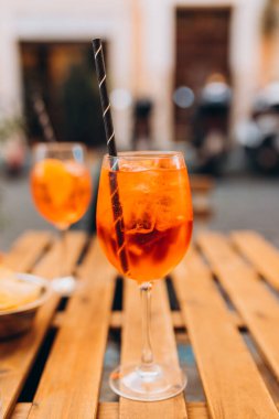 Aperol Spritz Kokteyli. Açık havada buz küpleri olan masaya dayalı alkollü içecek. Portakal dilimi ve samanla servis edilen kokteyl İtalya 'daki kaldırım kafenin ahşap masasına kondu.