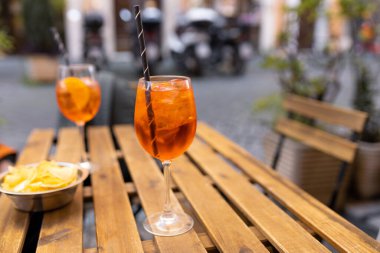 Aperol Spritz Kokteyli. Açık havada buz küpleri olan masaya dayalı alkollü içecek. Portakal dilimi ve samanla servis edilen kokteyl İtalya 'daki kaldırım kafenin ahşap masasına kondu.