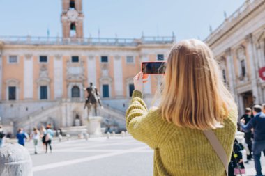 Akıllı telefonlu sarışın kadın güneşli bir günde yürüyor. Capitol Roma 'da, Piazza del Campidoglio Capitoline Hill, İtalya' da. Seyahat eden ünlü simgeler kavramı.