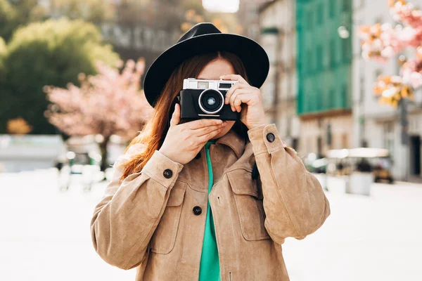 カメラで彼女の顔を覆う写真家の肖像 通りの背景にポーズバックパック付きのケアフリー女性 積極的な観光客屋外 陽気な30代の女の子で帽子あります探検都市 — ストック写真