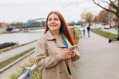 Hippi kızıl saçlı kadın akıllı telefondan ya da teknolojiden mesaj atıyor, turist kadın elleri bulanık şehir arka planında alet tutuyor.