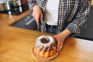 Mutfaktaki tahta masada çikolatalı bademli pasta kesen bir kadın. Mutfak, yemek pişirme ve yemek pişirme konsepti