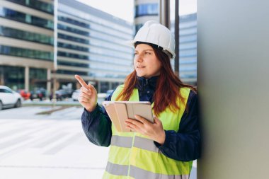 Uzman müfettişler dizüstü bilgisayarla ve inşaat alanında dijital tablet kullanan kadın mühendisle ilgili planlar yapıyorlar.