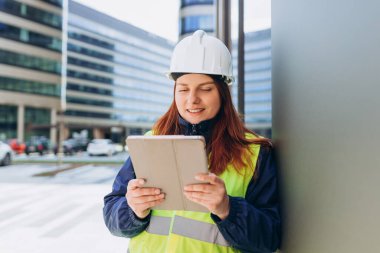 Kadın mühendis ya da mimar tabletle dışarıda duruyor. İnşaat alanında çalışırken güvenlik kaskı takan bir müfettiş. Başarılı ve gururlu müfettiş..