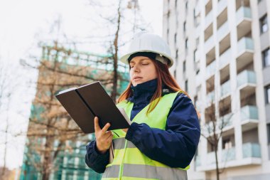 İnşaat alanında evrakları olan kağıt klasörlü bir mimar. Beyaz kask takan başarılı kadın müteahhit portresi ve güvenli sarı yelek. Kadın yeni bir inşaat projesi planlıyor..
