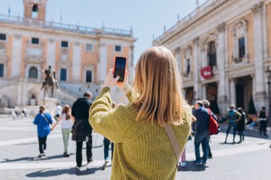 Akıllı telefonlu sarışın kadın güneşli bir günde yürüyor. Capitol Roma 'da, Piazza del Campidoglio Capitoline Hill, İtalya' da. Seyahat eden ünlü simgeler kavramı.