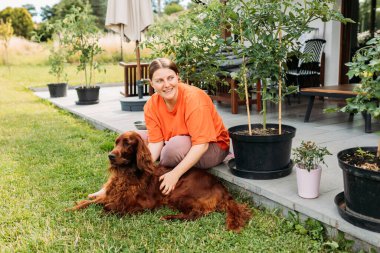 Yazın evin bahçesinde köpeğiyle oynayan neşeli, mutlu genç bir kadın. Güzel İrlandalı yerleşimci köpek çimenlerde yatıyor.