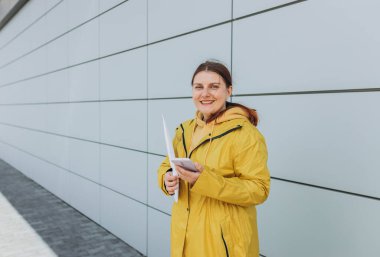 Sarı üniformalı genç bir kadın akıllı telefon kullanıyor ve paketi tutuyor. Teslimat servisi bir paket mektup gönderdi.