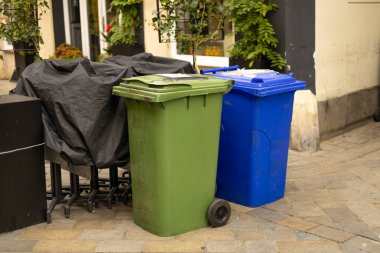 Yolun kenarındaki çöp yığını. Plastik yeşil ve mavi tekerlekli çöp bidonları çöp toplama için yol kenarındaki çöp bidonları.