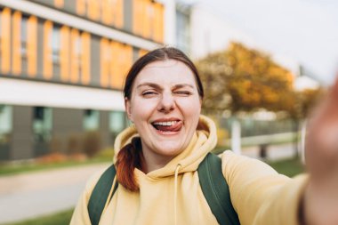 Genç ve mutlu bir kadın, şehir caddesinde bir kamerada selfie çekiyor. Dışarıdaki telefonla görüntülü konuşma yapan bir kız..