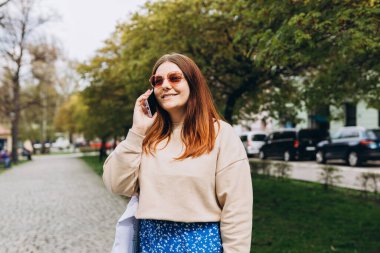 Sokakta poz veren bir kadının açık hava moda portresi. Açık havada akıllı telefon kullanan bir kadına yakın çekim. Kentsel yaşam tarzı konsepti