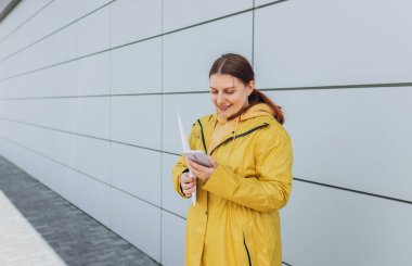 Sarı üniformalı genç bir kadın akıllı telefon kullanıyor ve paketi tutuyor. Teslimat servisi bir paket mektup gönderdi.