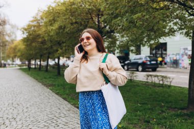 Sokakta poz veren bir kadının açık hava moda portresi. Açık havada akıllı telefon kullanan bir kadına yakın çekim. Kentsel yaşam tarzı konsepti