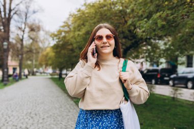 Sokakta poz veren bir kadının açık hava moda portresi. Açık havada akıllı telefon kullanan bir kadına yakın çekim. Kentsel yaşam tarzı konsepti
