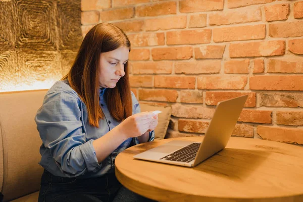 Indoor shot of young woman holding papers in her hands, calculating family budget. Young busy business woman manager working in office with laptop