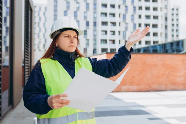 Angry female construction worker in hardhat with folder outdoors. Woman construction worker in hard hat crazy and mad shouting and yelling with aggressive expression and arms raised.