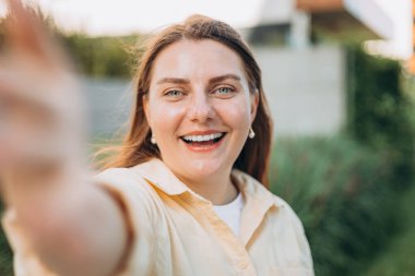 Genç ve mutlu bir kadın, şehir caddesinde bir kamerada selfie çekiyor. Şehir hayatı konsepti. Dışarıdaki telefonla görüntülü konuşma yapan bir kız..