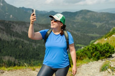 Bir kadın dağlarda telefon sinyali bulmaya çalışıyor. Tatilde vahşi doğada mobil bağlantı aranıyor. Kızgın kadın turist yürüyüşçüsü akıllı telefon arama sinyali tutuyor.