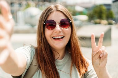 30 'ların güzel kızı barış işareti ile poz veriyor. Gülen genç bir kadın şehrin arka planında selfie çekiyor..