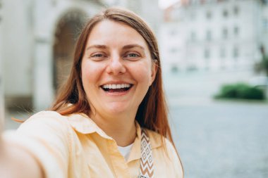 Çekici, sevimli, kısa saçlı, çekici bir kadının fotoğrafı. Kollar çapraz, kendine güvenen, arkadaş canlısı, gülümseyen, keyifli, ofis gömleği kentsel arka planda duruyor.