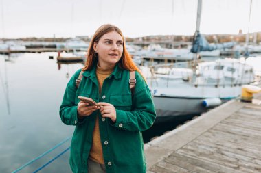 Akıllı telefonlu mutlu turist kız Avrupa 'ya seyahat ediyor. Kiralık tekneyle seyahat etmek için ilginç yerleri keşfederek tatil kavramı. Mekan arayan bir kadın, rıhtım boyunca yürüyor, deniz kenarında..