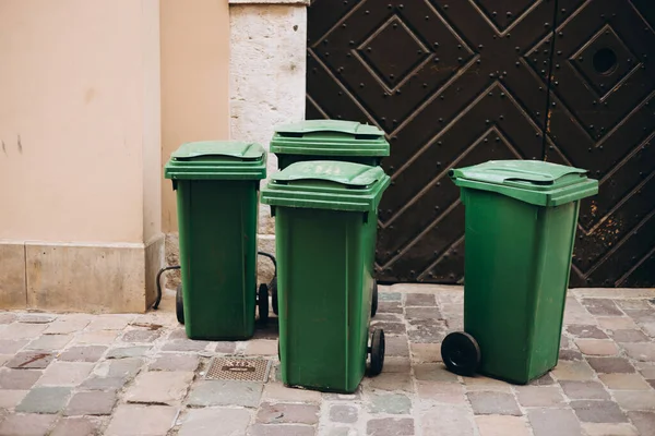 Public trashes on the side of the road. Plastic green wheeled recycling rubbish bins beside the road for rubbish collection.