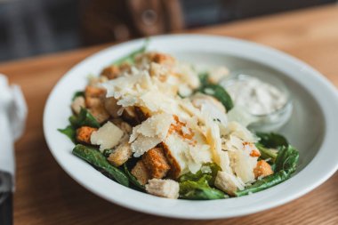 İçinde kızarmış ekmek, tavuk ve parmesan peyniri olan beyaz bir kase dolusu Cezar salatası.