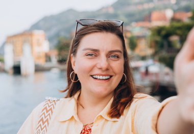 Fotoğraf gevşetici, pozitif kadın kamerayı tut ve dışarıda selfie çek. Tatil ve seyahat kavramı. Varenna, İtalya, Como