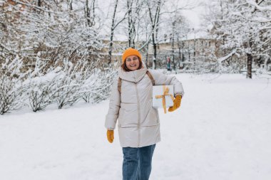 Gülümseyen şık orta yaşlı kadının portresi. Kışın şehir parkının dışında duruyor. 30 'lu yaşlardaki genç kadınlar Noel hediyelerini açık havada, tüm vücutlarıyla taşıyorlar.