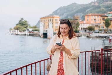 Akıllı telefonlu mutlu esmer kadın yaz tatilinin tadını çıkarıyor. Tatil ve seyahat kavramı. Varenna, İtalya. Como Gölü