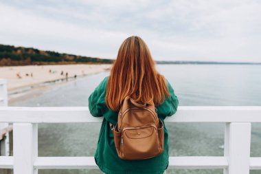 Sırt çantalı, deniz kenarında rahatlayan şık bir kadının arka görüntüsü. Özgürlük ve aktif yaşam tarzı kavramı. Yüksek kalite fotoğraf. Güç fikri, doğa.