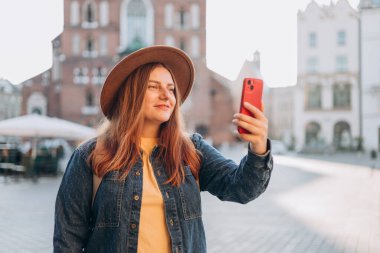 Krakow, Polonya 'daki pazar meydanında ünlü St. Marys Bazilikası' nın önünde selfie çeken şapkalı genç bir kadın. Sonbaharda Avrupa 'yı gezmek.