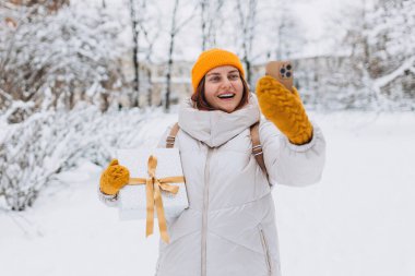 Winter City caddesinde sıradan kıyafetler içinde telefonunu kullanan güzel bir kadın. Şimdiki genç hippi doğada selfie çekiyor. Alışveriş kavramı, tatiller