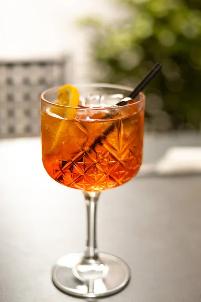 Aperol Spritz Cocktail. Alcoholic beverage based on table with ice cubes and oranges outdoors. Served cocktail with orange slice and straw placed on the table of sidewalk cafe