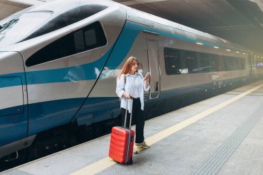 İstasyonda trende bekleyen genç mülteci kadın kaybetmiş ve akıllı telefon kullanmış. Gezgin. 30 'lu yaşlarda bavullu kadınlar tren istasyonunda yürüyor. Tatile trenle git.