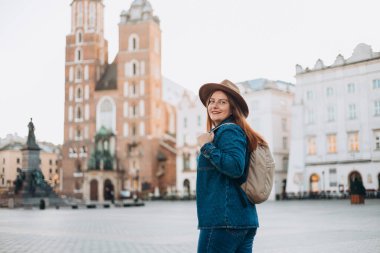 Çekici genç bayan turist yeni şehri keşfediyor. Krakow 'daki Pazar Meydanı' nda poz veren kızıl saçlı kız. Yazın seyahat. Aziz Mary Bazilikası. Tatil kavramı