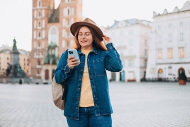 Çekici genç bayan turist yeni şehri keşfediyor. Krakow 'daki Market Meydanı' nda elinde akıllı bir telefon tutan kızıl saçlı kız. Yazın Avrupa 'yı geziyorum. Aziz Mary Bazilikası.