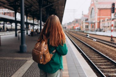 Tren istasyonunda küçük sırt çantalı, 30 'lu yaşlarda tren bekleyen genç bir kadın gezginin arka görüntüsü. Turizm, tek kişilik tatil, arka plan.