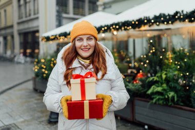 Hediye kutularını elinde tutan ve kış caddesinde gülümseyen mutlu, genç ve heyecanlı bir kadın. Kış tatili indirimi. Alışveriş, tatil ve noel kavramı.