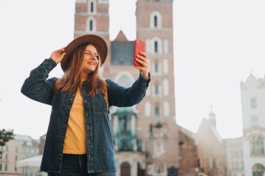 Krakow, Polonya 'daki pazar meydanında ünlü St. Marys Bazilikası' nın önünde selfie çeken şapkalı genç bir kadın. Sonbaharda Avrupa 'yı gezmek.