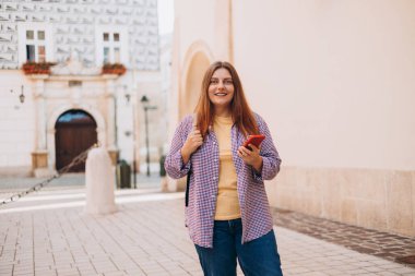 Sokakta elinde telefonla bekleyen güzel bir genç kadının fotoğrafı. Eski şehir caddesinde yürüyen 30 'ların turisti akıllı telefonunu kontrol ediyor. Teknoloji kavramı kullan