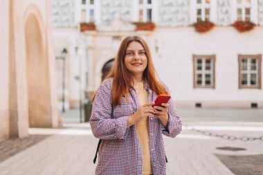 Sokakta elinde telefonla bekleyen güzel bir genç kadının fotoğrafı. Eski şehir caddesinde yürüyen 30 'ların turisti akıllı telefonunu kontrol ediyor. Teknoloji kavramı kullan