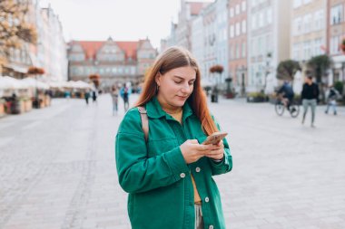 Sırt çantalı mutlu genç kadın akıllı telefonunu kontrol ediyor. Açık havada akıllı telefon kullanan 30 'lu yaşlardaki güzel bir kızın portresi. Kentsel yaşam tarzı afişi
