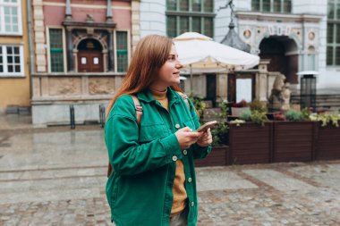 Sırt çantalı mutlu genç kadın akıllı telefonunu kontrol ediyor. Açık havada akıllı telefon kullanan 30 'lu yaşlardaki güzel bir kızın portresi. Kentsel yaşam tarzı afişi