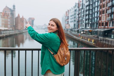 Çekici genç bayan turist yeni şehri keşfediyor. Gdansk 'taki şehir caddesinde sırt çantalı, kızıl saçlı bir kız. Sonbaharda Avrupa 'yı geziyorum. Meşhur Zuraw Turnası, Motlawa Nehri