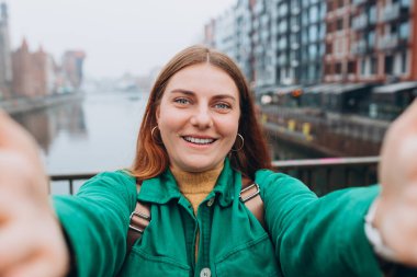 Mutlu 30 'lu yılların kadınları kentin arka planında selfie çekiyor. Genç güzel kız merhaba diyor. Gdansk eski kasabası ve ünlü Zuraw vinci Motlawa nehrinin yanında güzel bir kadın duruyor.