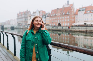 Genç mutlu kızıl saçlı kadın şehirde cep telefonuyla arama yapıyor. Şehirdeki orta yaşlı bir kadın akıllı telefondan konuşuyor.