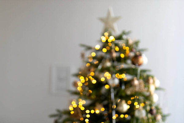 Blurred background of dressed up Christmas tree. Christmas banner with copy space, blurred lights, highlights. Defocus golden abstract background